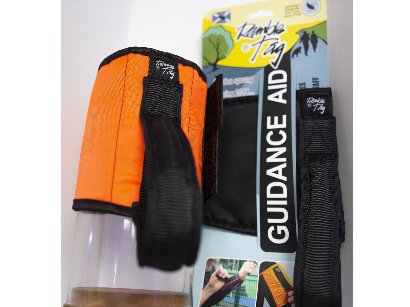 Ramble tag shown in orange water resistant fabric, consisting of a velcro cuff that can be wrapped around the upper arm and fasten with the two velcro straps at the end, and a grip handle user can hold on to as the wearer moves.